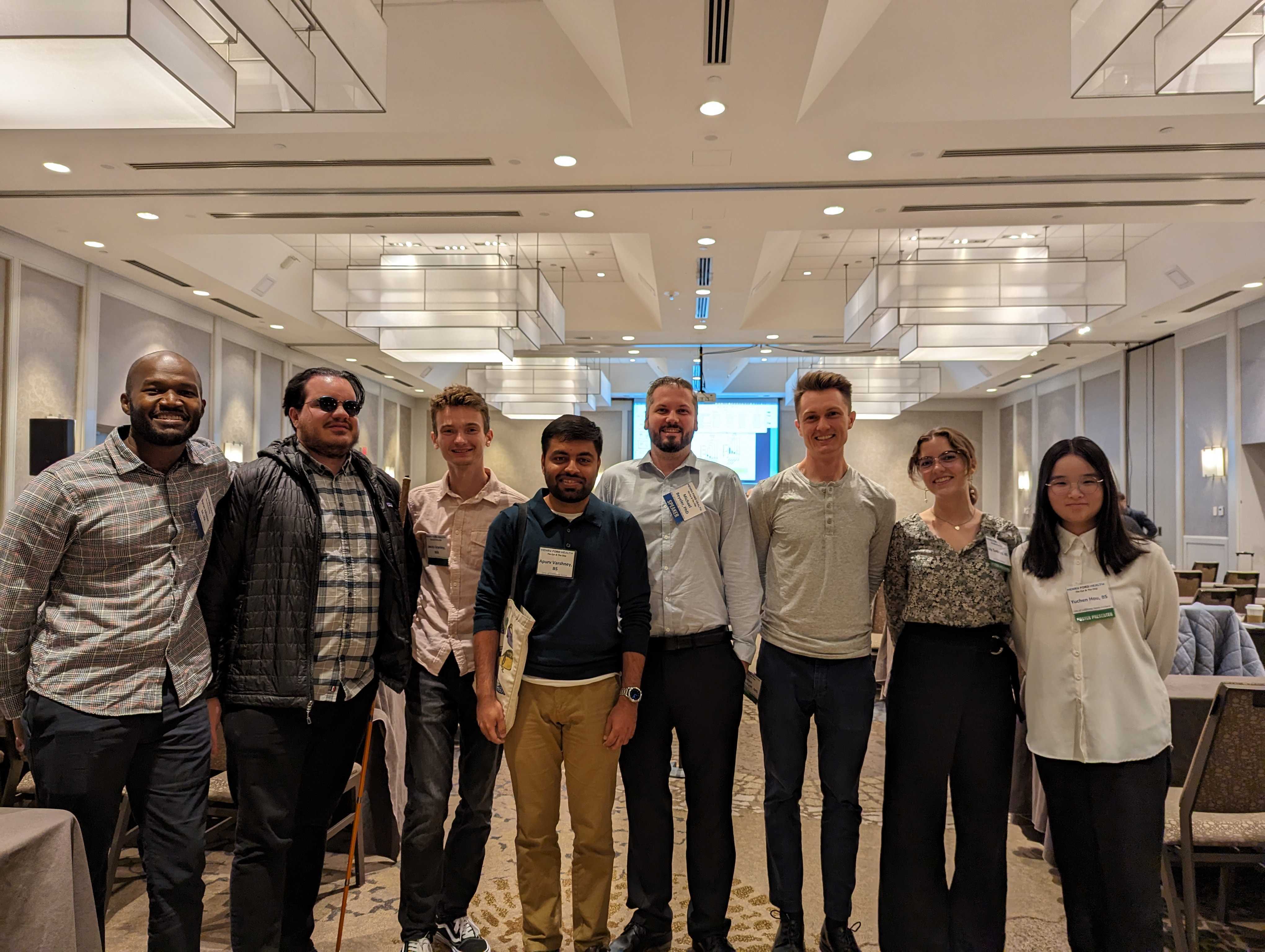 Eight lab members with conference name badges stand together in a hotel ballroom at The Eye and the Chip World Congress on Artificial Vision. From left to right: Byron Johnson, Lucas Nadolskis, Jacob Granley, Apurv Varshney, Prof. Beyeler, Galen Pogoncheff, Lily Turkstra, and Yuchen Hou.